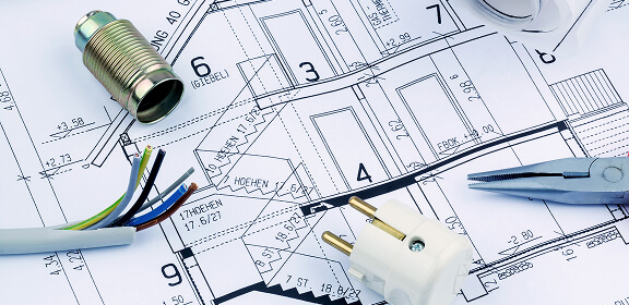Electrical tools and plug on architectural blueprints. Plier, plug connector, and multicolored wires placed diagonally on technical drawings.